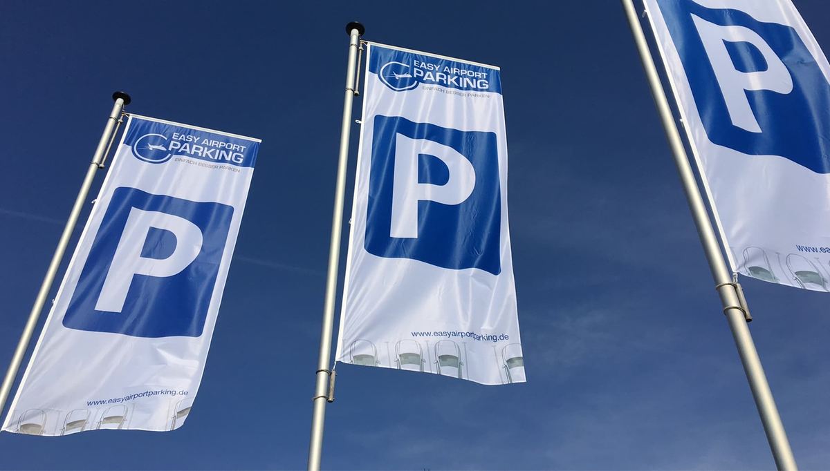 Drei Fahnen mit Easy Airport Parking Logo und Parkplatzsymbol auf dem Parkplatz von Easy Airport Parking am Flughafen Eindhoven (EIN)