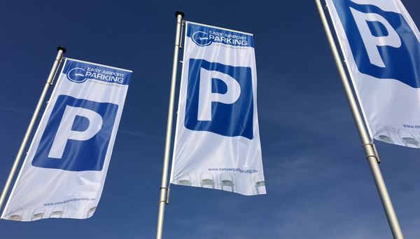 Tre flag med Easy Airport Parking-logo og parkeringssymbol på parkeringspladsen hos Easy Airport Parking ved Eindhoven Lufthavn (EIN)